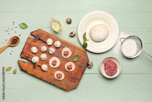 Board with uncooked dumplings and ingredients on green wooden background