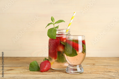 Mason jar and glass of fresh lemonade with strawberry on wooden table