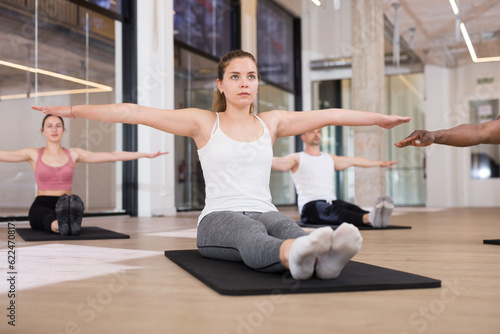 Focused woman exercising pilates with group of young adult sporty people at fitness center