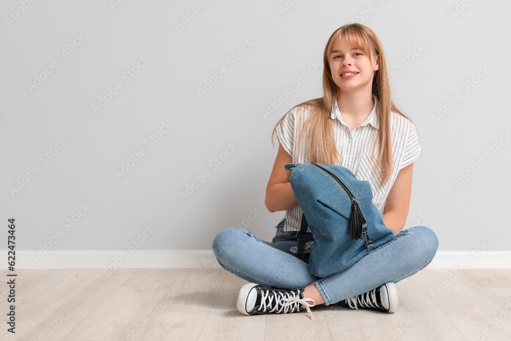 Female student with backpack sitting near light wall