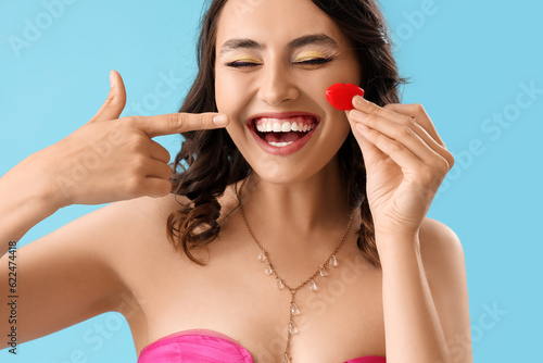 Happy young woman pointing at candy in shape of lips on blue background  closeup