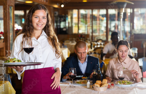 Successful young waitress standing in restaurant with ordered meals  ready to serving guests