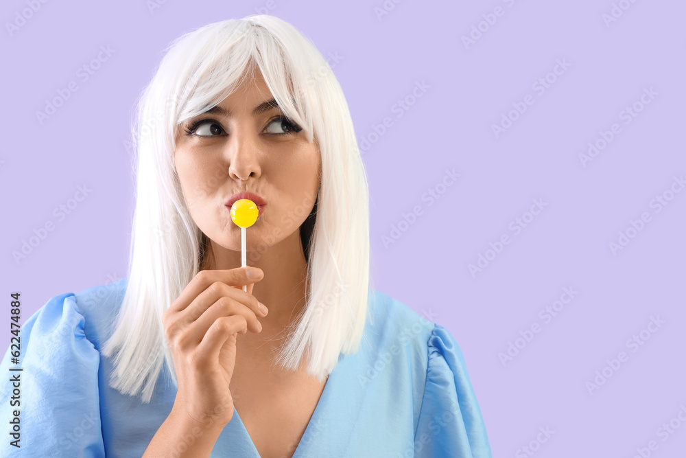 Young woman in wig eating lollipop on lilac background, closeup Young woman in wig eating lollipop on lilac background, closeup