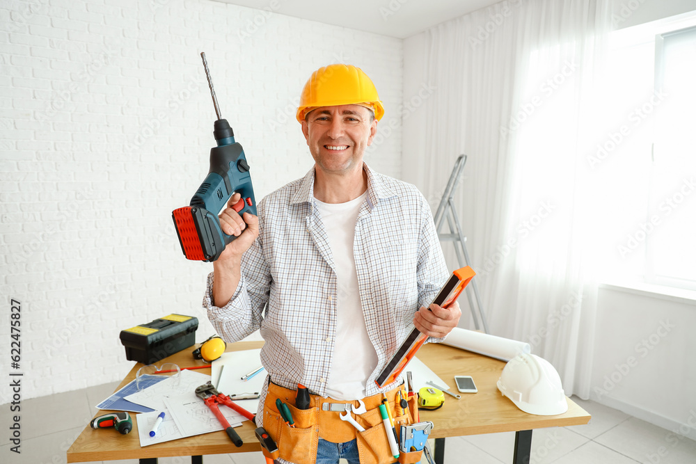 Mature builder with drill and level in room Mature builder with drill and level in room