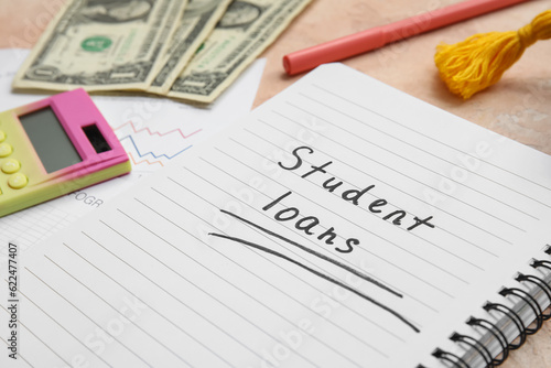 Notebook with text STUDENT LOANS, dollar banknotes and stationery on beige table