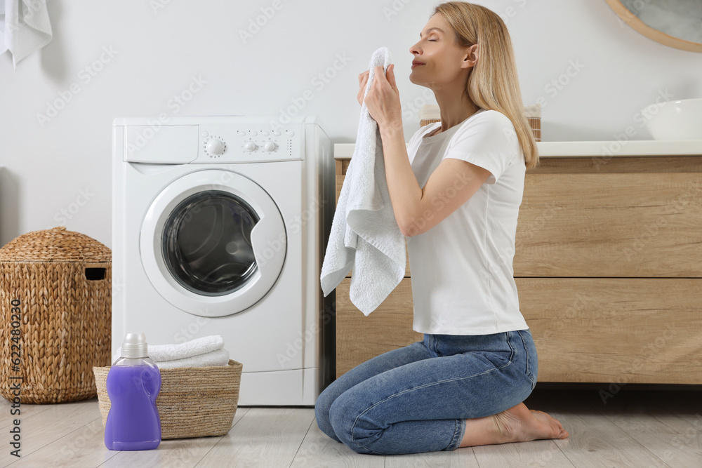 Woman smelling clean towels and sitting on floor near washing machine in bathroom, space for text Woman smelling clean towels and sitting on floor near washing machine in bathroom, space for text