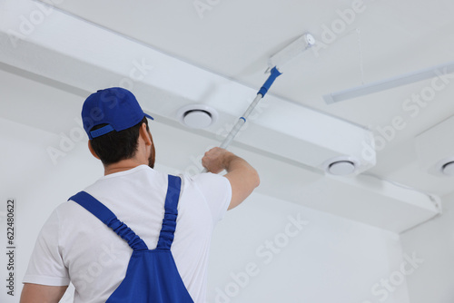 Handyman painting ceiling with roller in room  back view