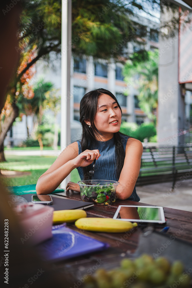 University student eating a salad while taking a break from classes. She is at the college campus.