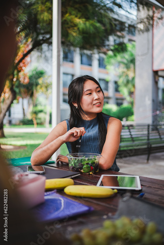 University student eating a salad while taking a break from classes. She is at the college campus.