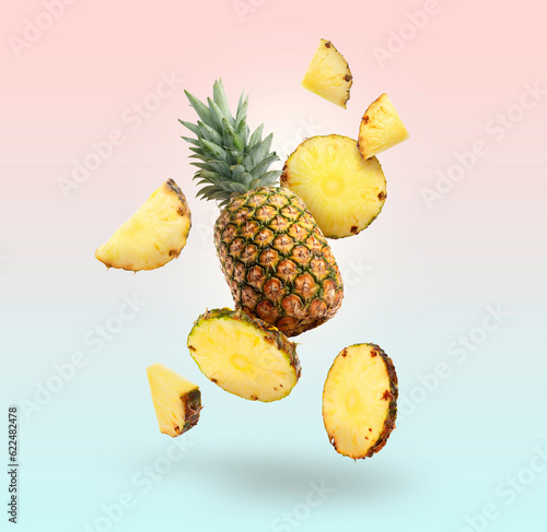 Fresh whole and cut pineapples falling on colorful background