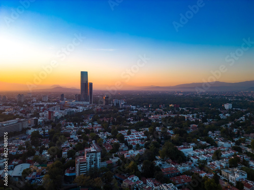 Aerial view of amazing sunrise over modern city with skyscraper of Mexico City with tall Mitikah Tower at bright orange sunrise with blue sky over foggy mountains in morning time