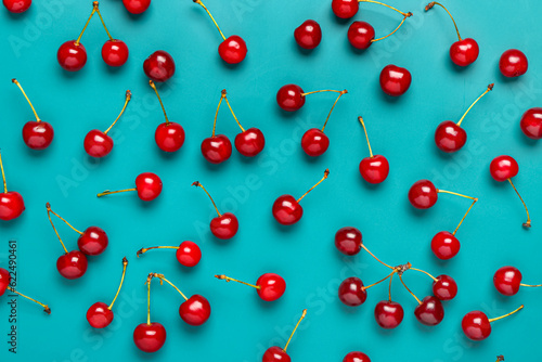Obraz na płótnie Fresh red cherries scattered on a vibrant teal background, healthy fruit and sum