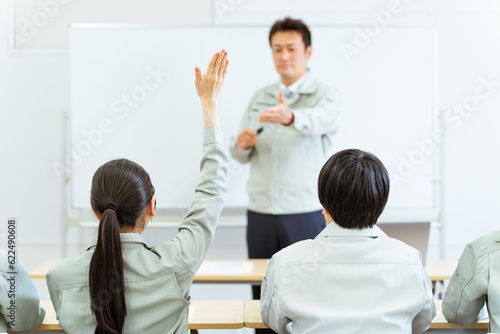 会議室で講習・セミナーを受ける挙手をして質問する女性の後ろ姿
