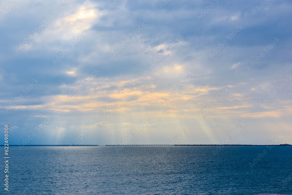 On a clear summer day, the sunset sun shines through the clouds and onto the sea On a clear summer day, the sunset sun shines through the clouds and onto the sea