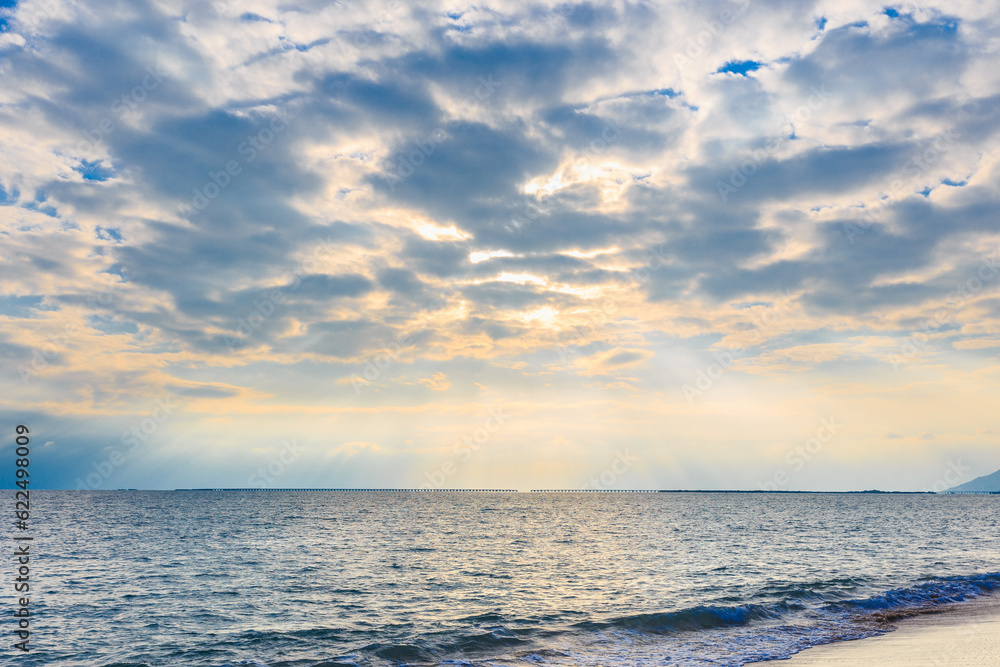 On a clear summer day, the sunset sun shines through the clouds and onto the sea