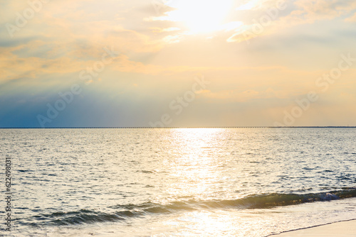 On a clear summer day  the sunset sun shines through the clouds and onto the sea