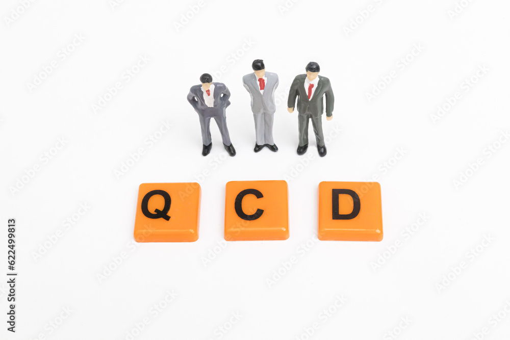 Three miniature businessman look at the QCD word. QCD print screen on orange plate. The concept of Quality, Cost, Delivery. The concept of QCD Analysis. business and Strategy concept. Three miniature businessman look at the QCD word. QCD print screen on orange plate. The concept of Quality, Cost, Delivery. The concept of QCD Analysis. business and Strategy concept.