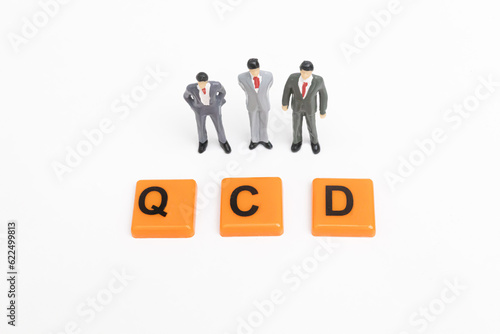 Three miniature businessman look at the QCD word. QCD print screen on orange plate. The concept of Quality, Cost, Delivery. The concept of QCD Analysis. business and Strategy concept. photo