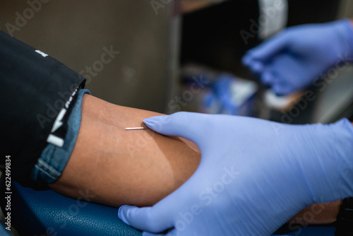 Close up hand doctor wearing rubber gloves injects a needle into a person's arm for blood transfusion
