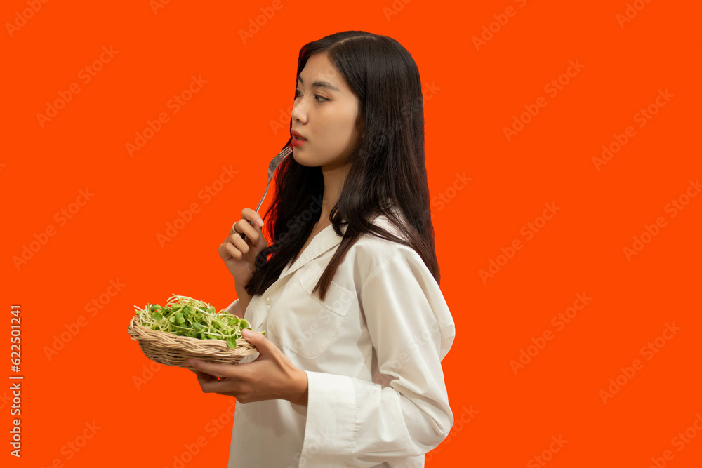 Vegetarian concept, Healthy woman eating sunflower sprouts standing isolated over orange background Vegetarian concept, Healthy woman eating sunflower sprouts standing isolated over orange background