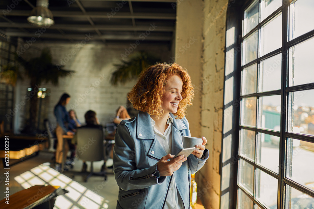 Young woman using a smart phone while looking through the window in a startup company office Young woman using a smart phone while looking through the window in a startup company office