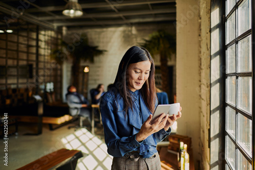 Photography Young woman using a smart phone while looking through the window in the office