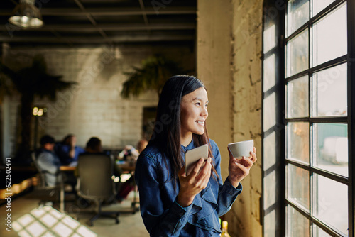 Wall Mural Young woman using a smart phone while looking through the window in the office