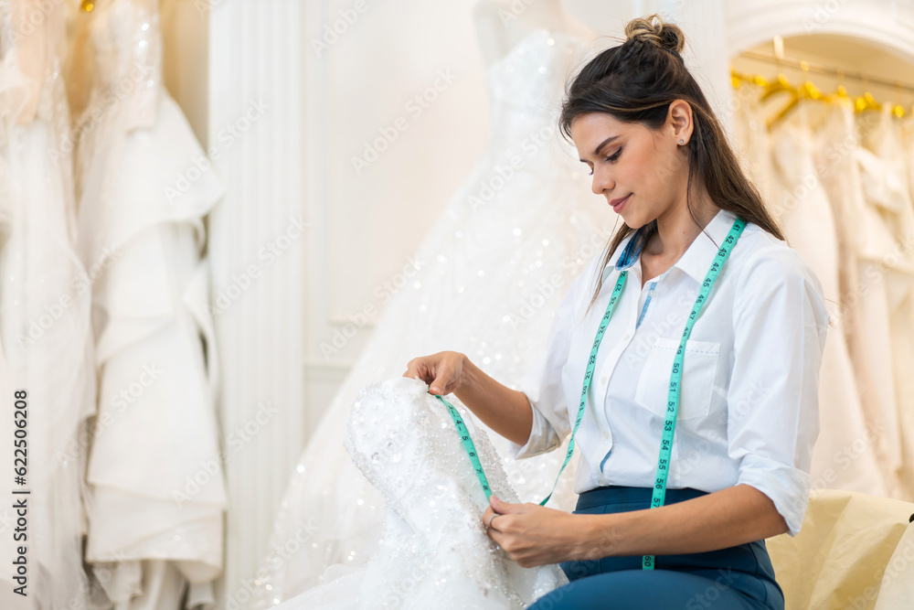 Obraz premium Portrait of entrepreneur bridal shop owner business woman fashion designer stylish working.Attractive designer girl using tape meter fitting on wedding dress with mannequin at wedding studio