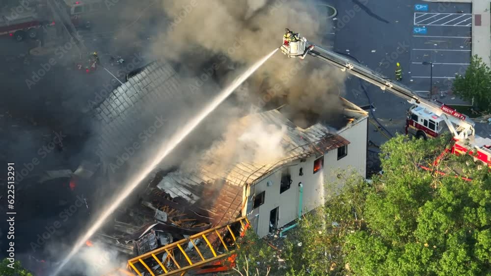 Firefighter on ladder spraying with water on burning building after explosion in american city - Aerial top down Firefighter on ladder spraying with water on burning building after explosion in american city - Aerial top down