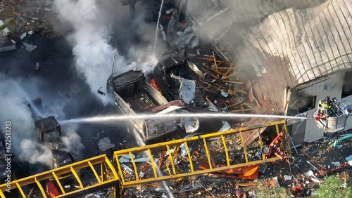 Aerial top down of firefighter spraying water with hose on burning vehicles after gas explosion - Panning shot