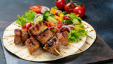 Healthy barbecued lean cubed pork kebabs served with a corn tortilla and fresh lettuce and tomato salad, close up view on a dark background