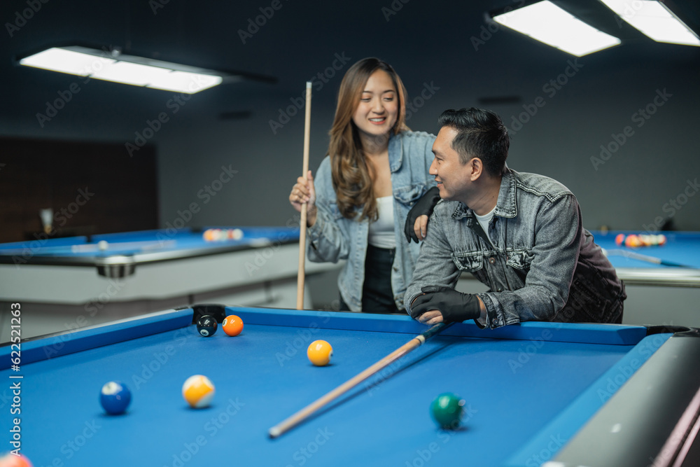 Fototapeta premium asian woman holding the cue stick while standing put her hand on the shoulder of her friends during the break