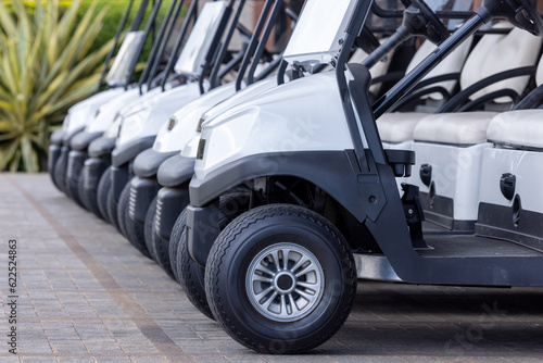  Golf cars in a row outdoors on a golf course. A row of empty golf carts on a golf course. golf course carts cars at luxury resort sport venue.All lined up ready for a tournament on a course.