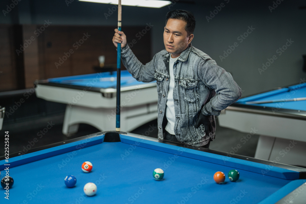 Fototapeta premium portrait of confuse pool player put his hand on his waist while observing the billiard balls