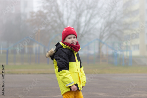 A little boy in a yellow jacket lost in the fog in the city.