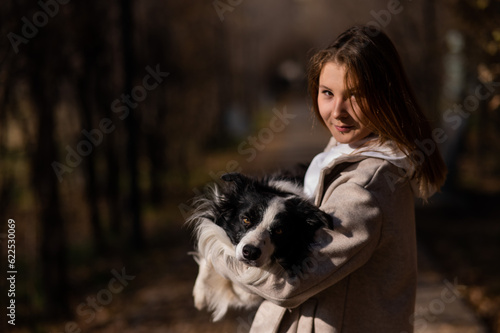 Caucasian woman holding a border collie in her arms while walking in the autumn park. Portrait of a girl with a dog.