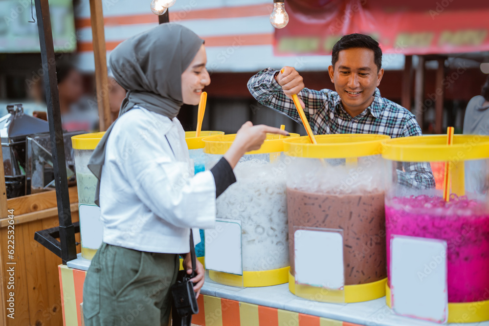 man sells colorful drink and juice in a jar to his female customer. street food vendor