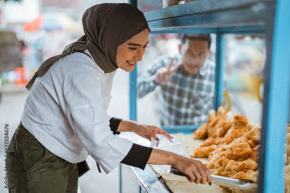 Fototapeta premium beautiful woman in hijab while sells various kinds of fried food with a cart on the side of the road