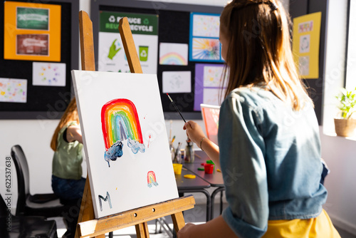 Happy diverse schoolchildren painting using brush and easel in school art class