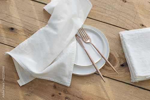 Empty white plate, golden cuterly and cotton napkin on wooden backdrop. photo