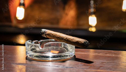 Foto Burning handmade luxury Cuban cigar resting on an ashtray on an old wooden count