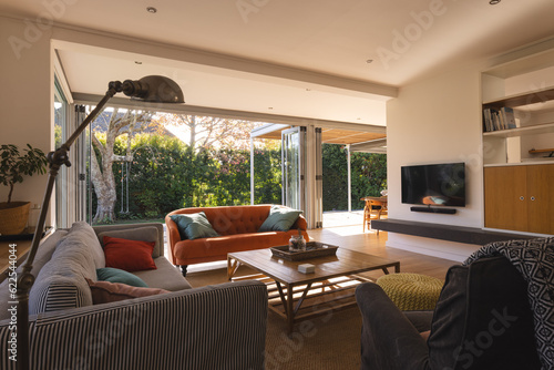 Interior of a living room with television, couch and armchair over big window and garden