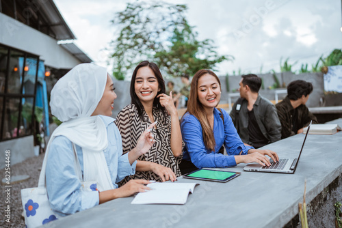 three Asian female students chat while working on a project together in an outdoor coworking space
