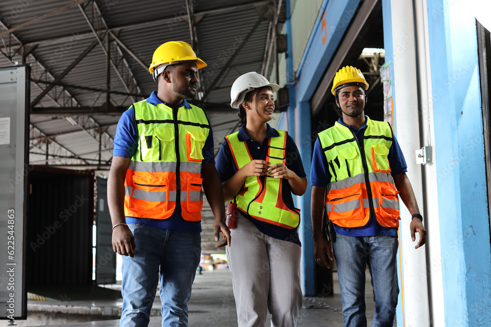 Group of warehouse workers with hardhats and reflective jackets using tablet, walkie talkie radio and cardboard while controlling stock and inventory in retail warehouse logistics, distribution center Group of warehouse workers with hardhats and reflective jackets using tablet, walkie talkie radio and cardboard while controlling stock and inventory in retail warehouse logistics, distribution center