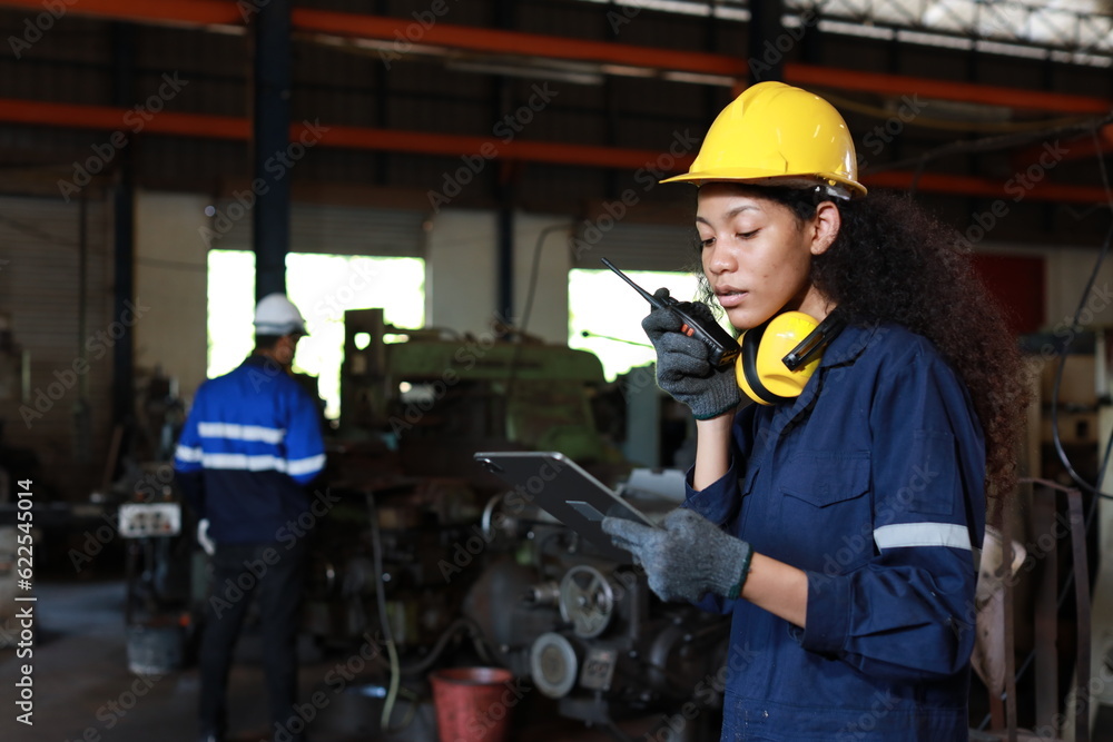Technician engineer or worker woman in protective suit using walkie talkie radio with tablet while controlling or maintenance operation work lathe metal machine at heavy industry manufacturing factory Technician engineer or worker woman in protective suit using walkie talkie radio with tablet while controlling or maintenance operation work lathe metal machine at heavy industry manufacturing factory