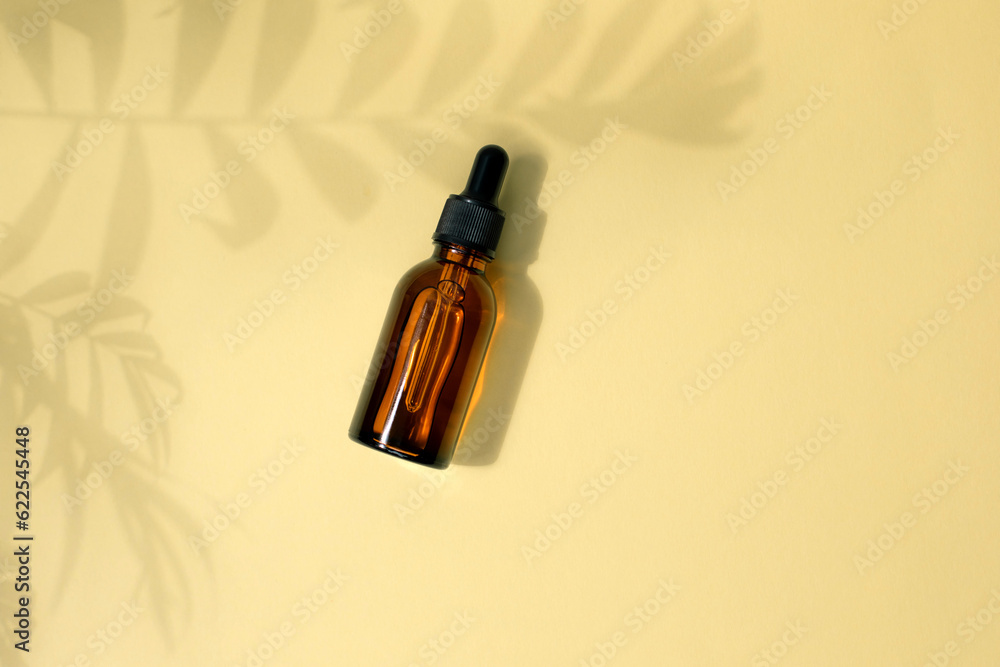 Amber bottle with facial treatment with a palm branch shadow on a yellow background. Top view Amber bottle with facial treatment with a palm branch shadow on a yellow background. Top view