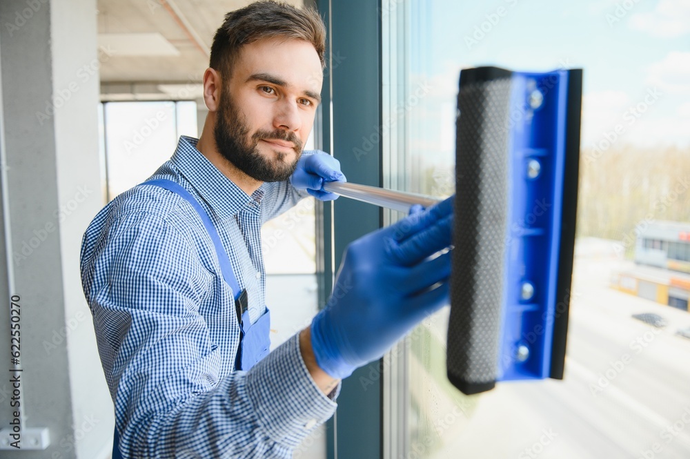 Young man cleaning window in office Young man cleaning window in office