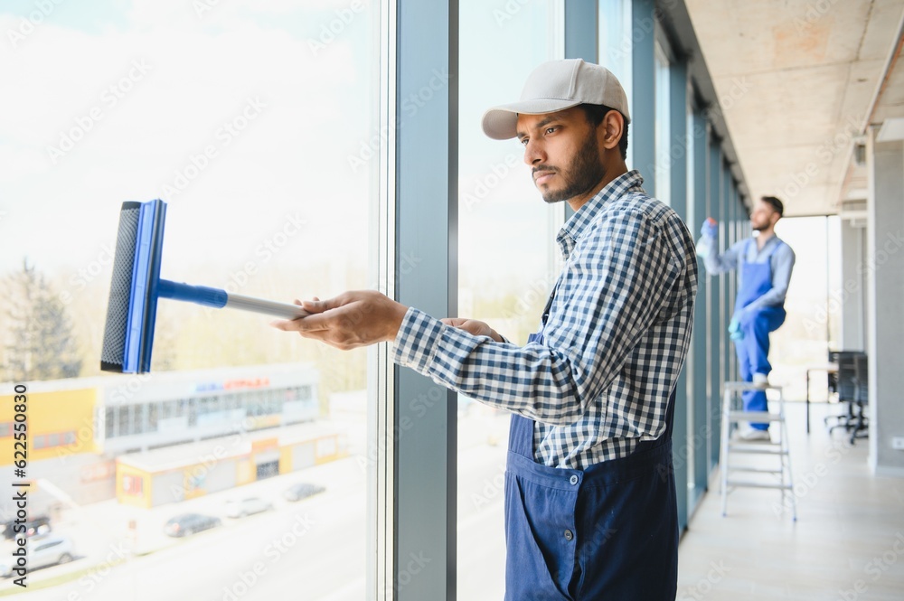 Young indian man washing window in office. Young indian man washing window in office.