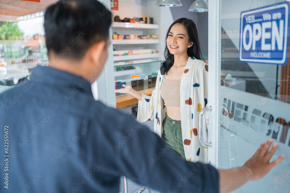 beautiful female shopkeeper smiling while welcoming the male customer at front of the store beautiful female shopkeeper smiling while welcoming the male customer at front of the store