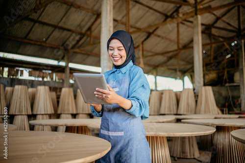 young businesswoman in veil standing using a tablet to work in wood craft shop